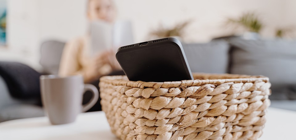 Basket with a phone on a table. A gray mug is in the background.