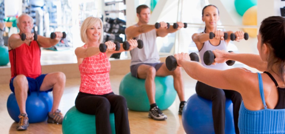 People sitting on a ball with bar bells in their hands