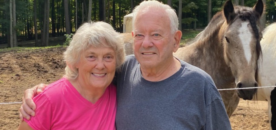 Man with his arm around a woman with horses in the background
