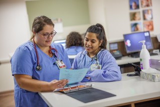 Two nurses talking about what's on the patient chart while standing at a counter
