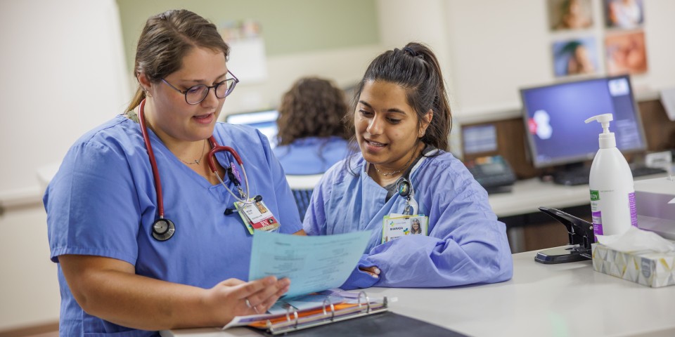 Two nurses talking about what's on the patient chart while standing at a counter