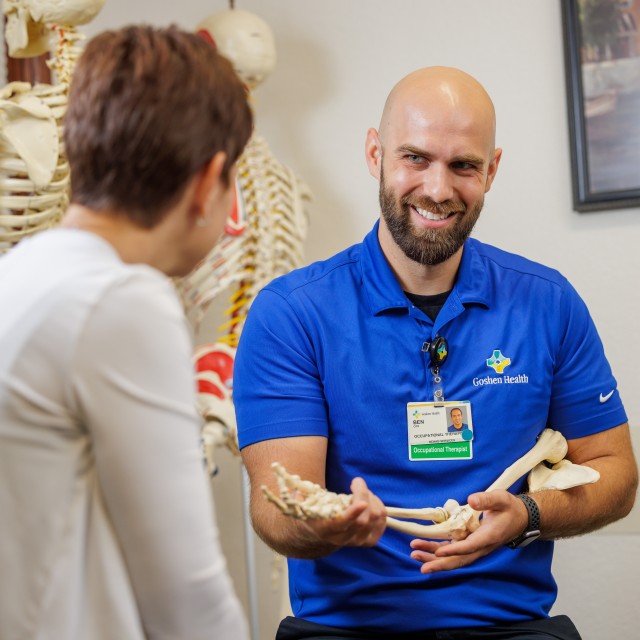 Rehabilitation therapist discussing care with a patient while holding a model of arm bones