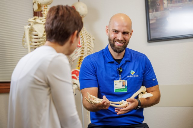 Rehabilitation therapist discussing care with a patient while holding a model of arm bones