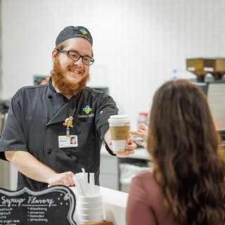 A Goshen Health Colleague standing in the coffee shop, handing a drink to a customer