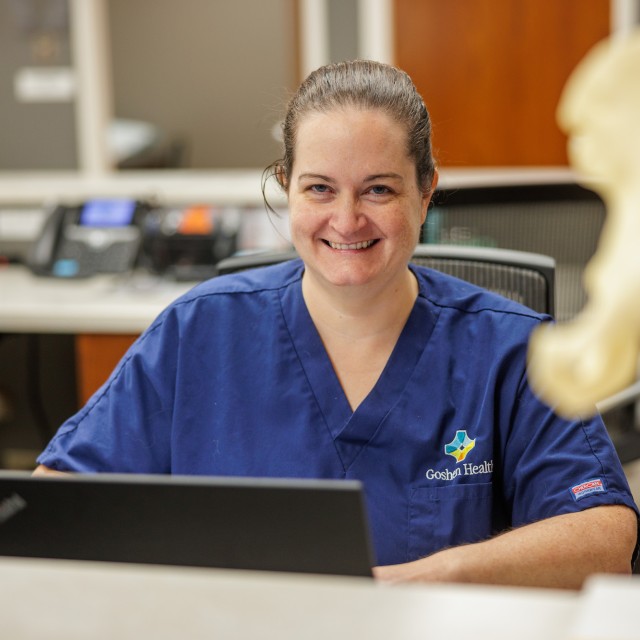Nurse sitting at a desk with a computer, smiling