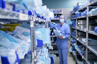 A nurse wearing a mask while pulling medical supplies from a shelf in the supply room