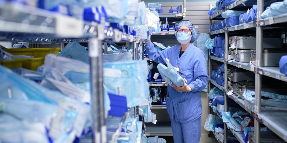 A nurse wearing a mask while pulling medical supplies from a shelf in the supply room