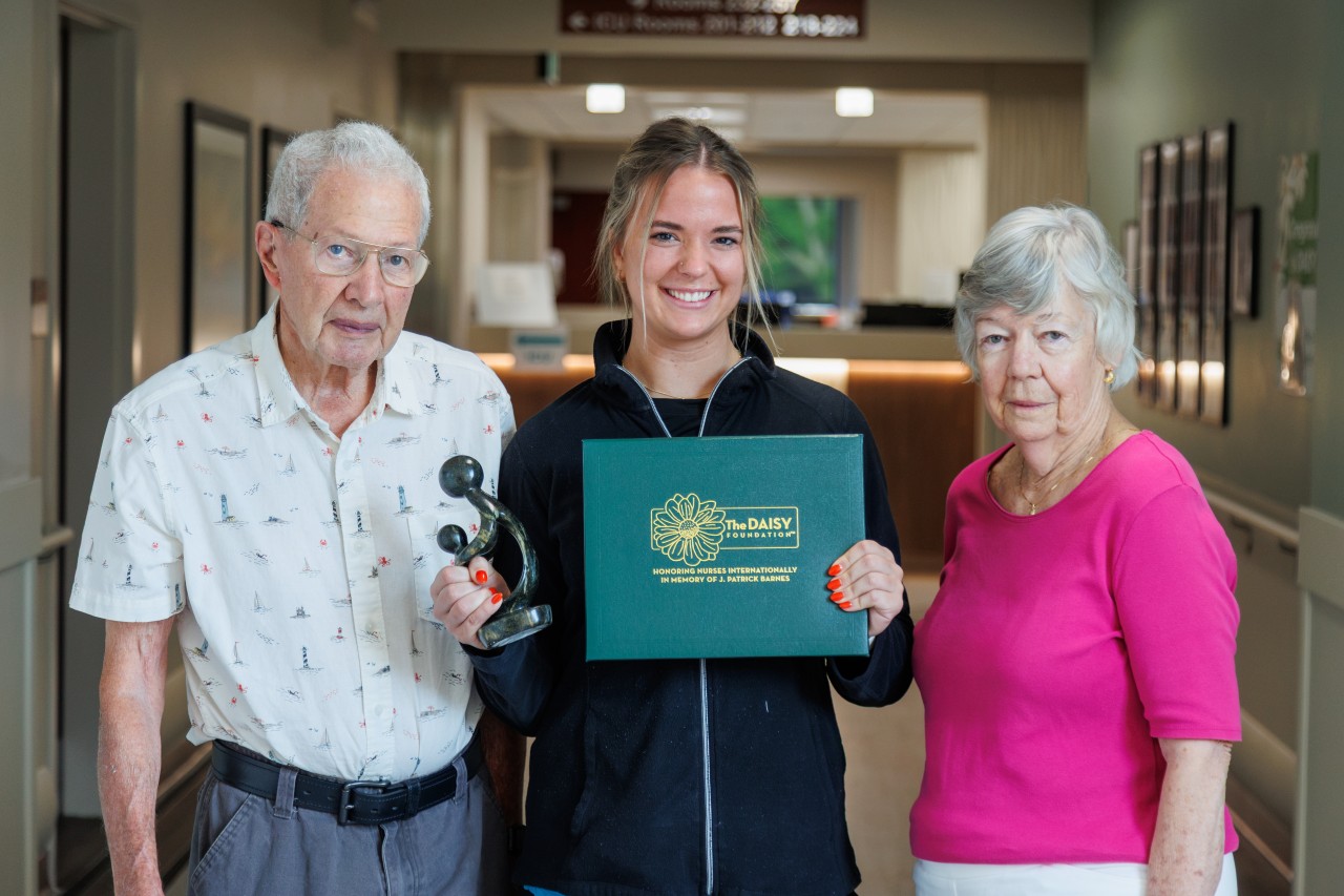 A young woman holding an award while standing between two older people