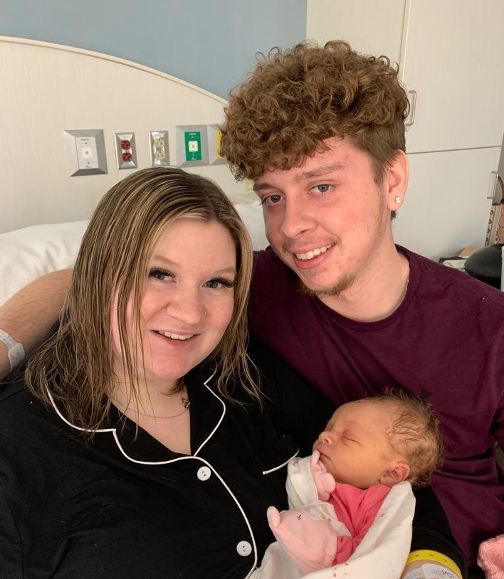 Man with his arm around a woman holding a newborn baby