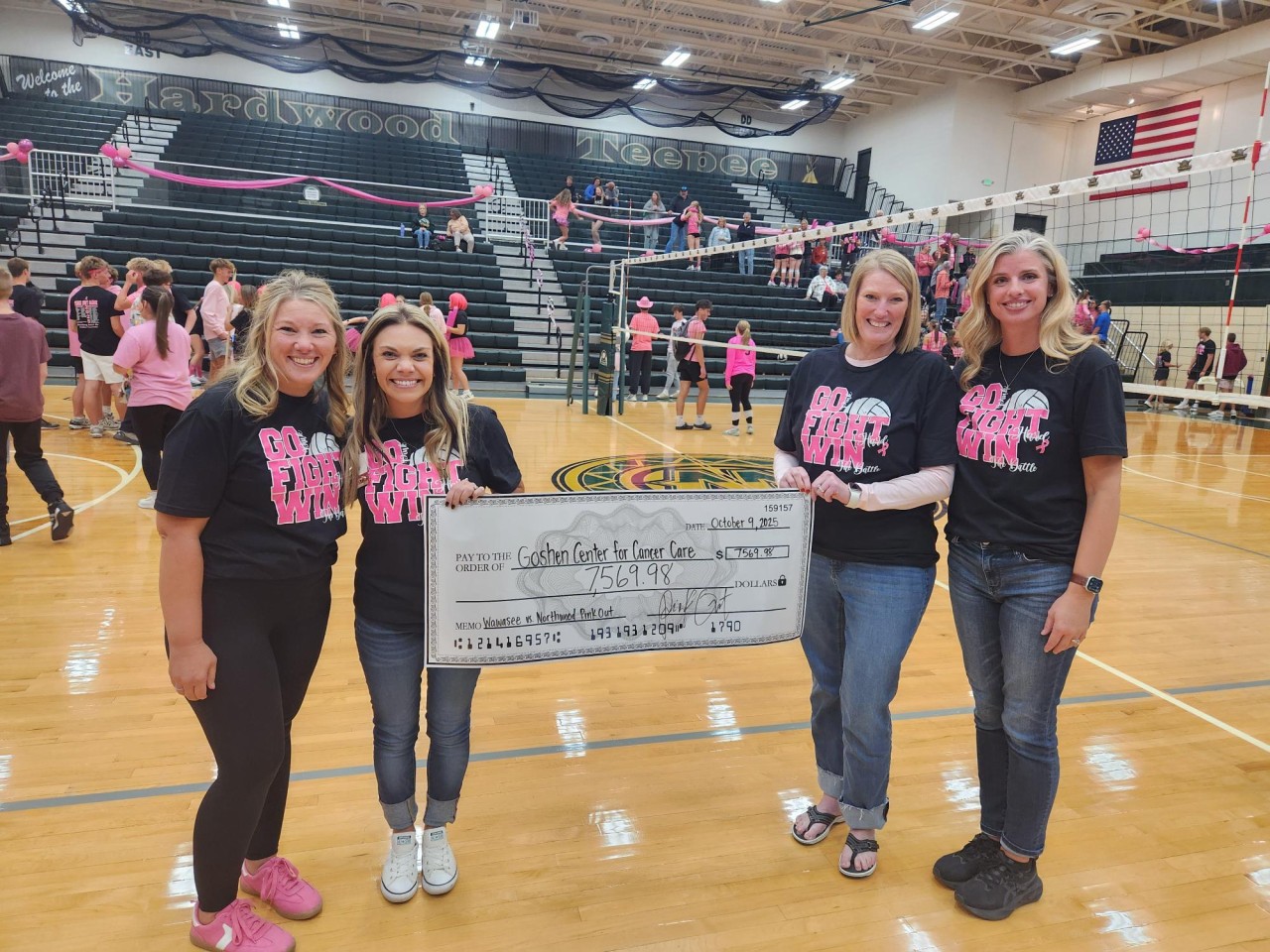 Ladies standing on a gym floor holding a check
