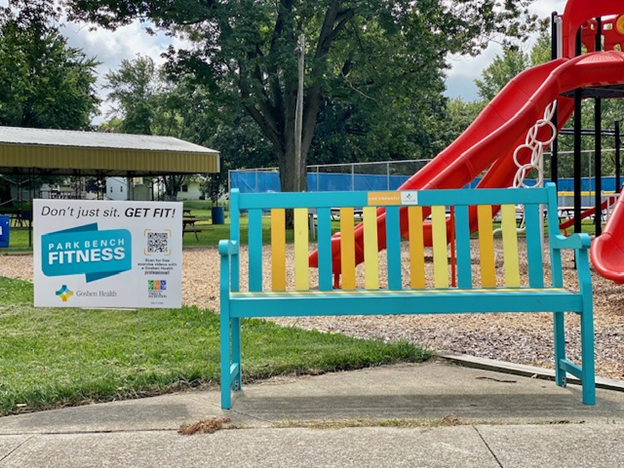 Sign in the yard next to a colorful bench at a park