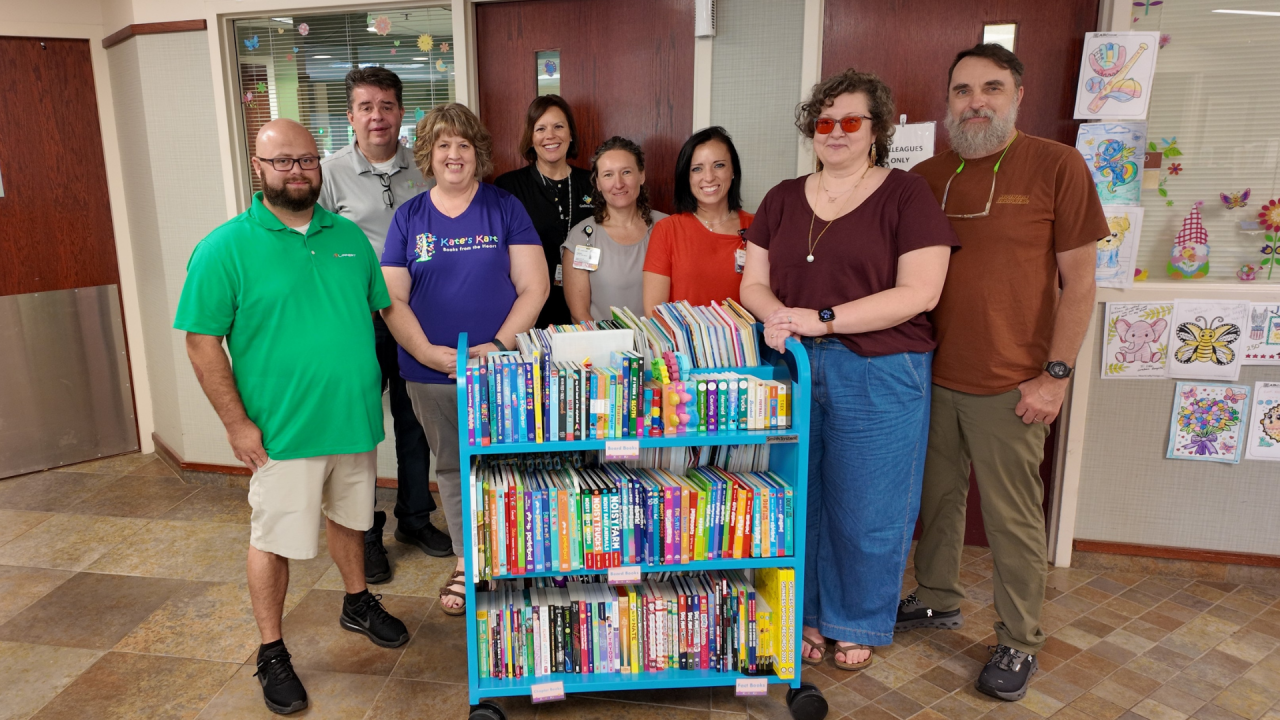 Several people standing around a cart of books for distribution at a hospital