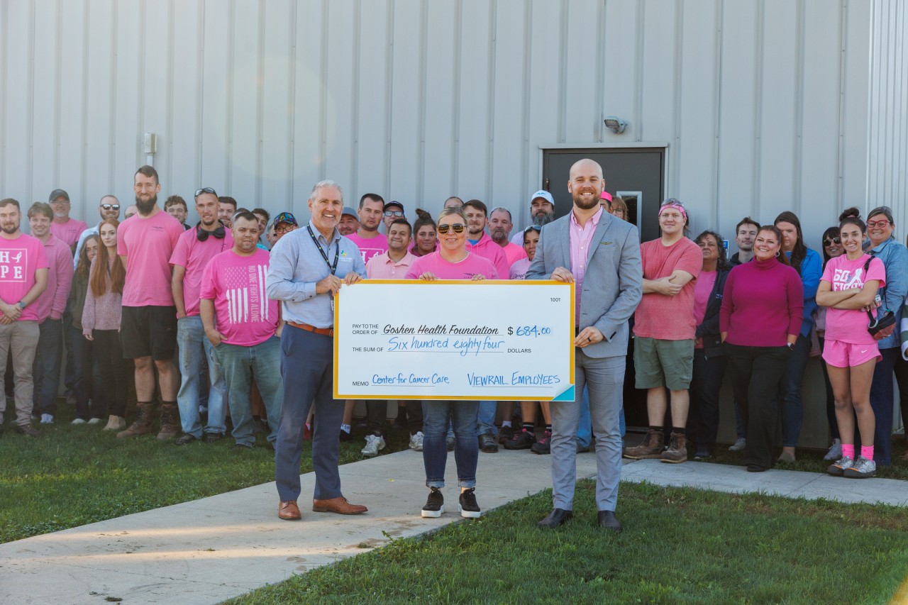 Two men holding a large check with employeeds behind them