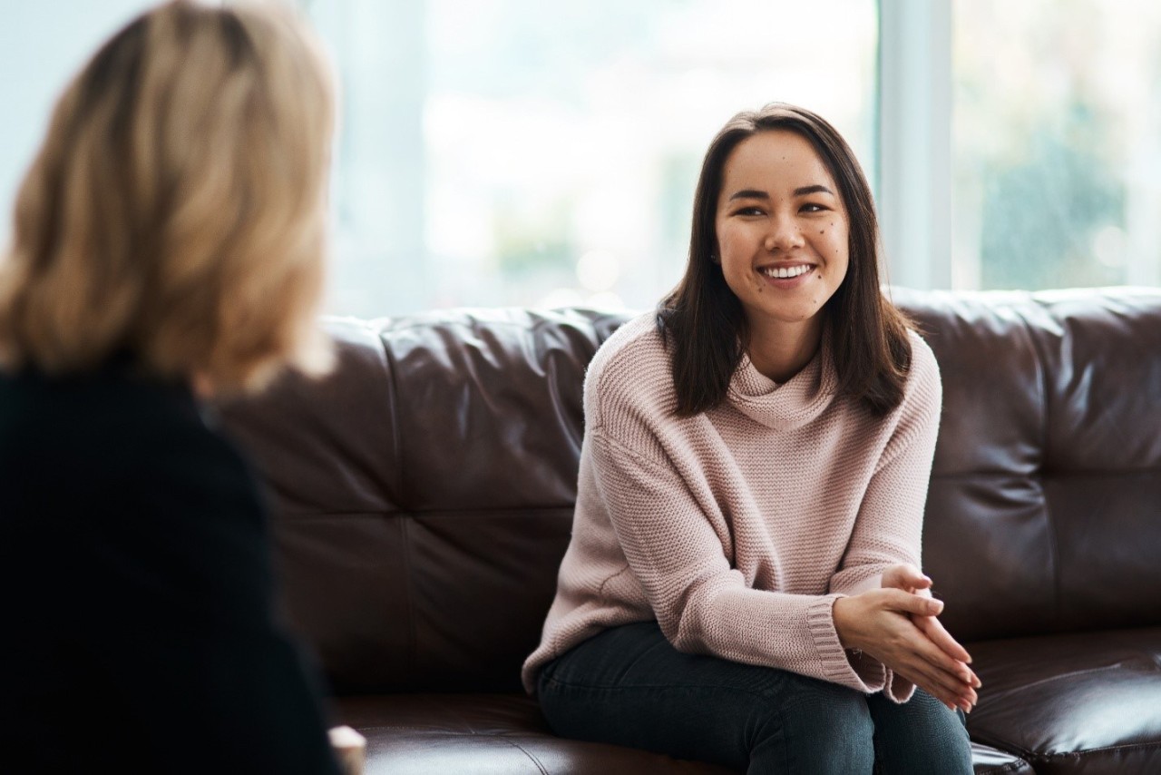 Woman sitting on a couch smiling while facing another woman