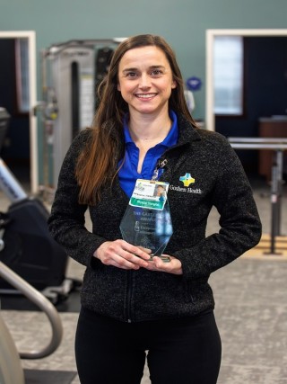 Woman standing and smiling while holding a trophy with both hands