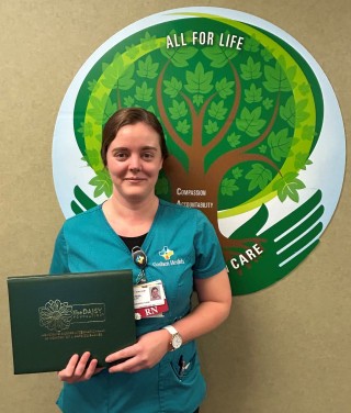 Woman standing in front of a tree picture holding an award