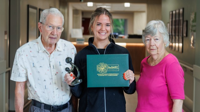 A young woman holding an award while standing between two older people
