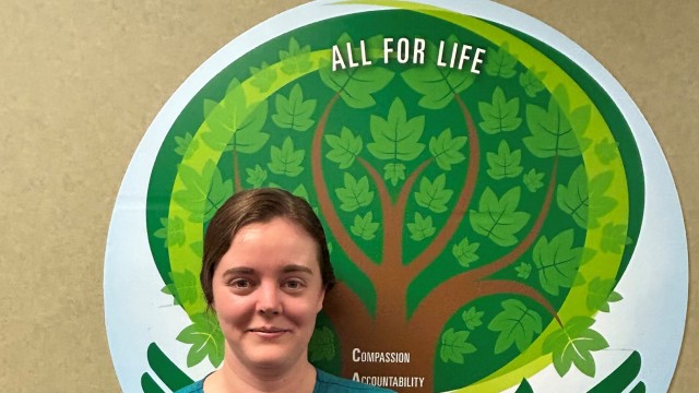 Woman standing in front of a tree picture holding an award