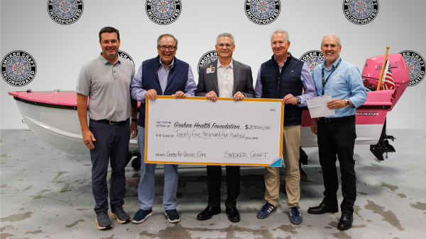 Five men smiling while holding a large check They are standing in front of a boat in a showroom
