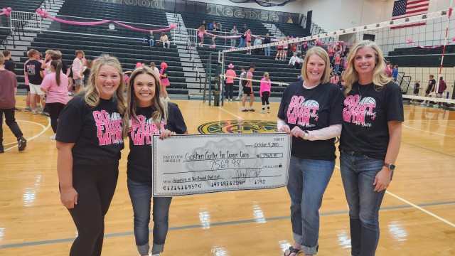 Ladies standing on a gym floor holding a check