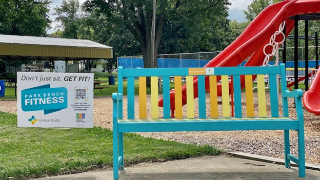 Sign in the yard next to a colorful bench at a park