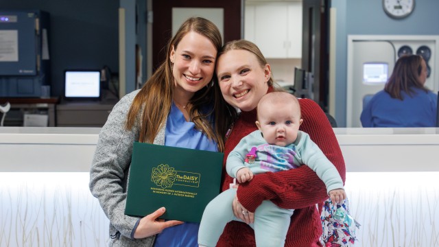 Two women holding a baby and an award