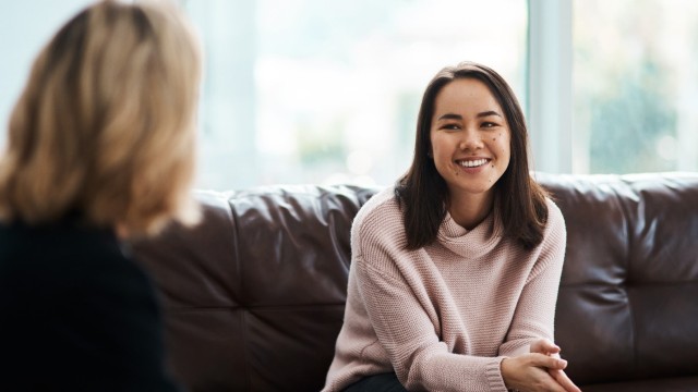 Woman sitting on a couch smiling while facing another woman