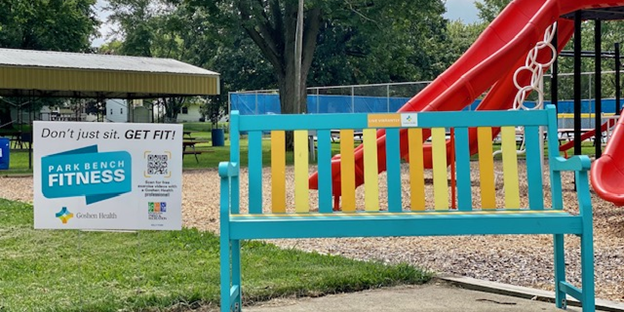Sign in the yard next to a colorful bench at a park