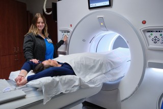 A technician helping a patient laying on a bed into a machine for scanning