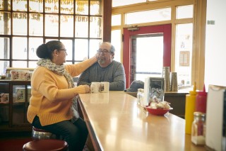 Woman sitting on stool at a counter with her hand on her husband's face
