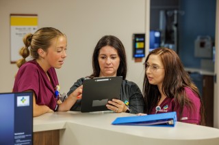 Three nurses discussing a chart while standing at the counter