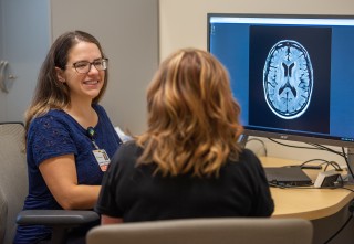 Doctor and patient sitting at a desk with a computer screening showing an image of a brain