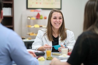 Woman sitting at a desk across from two people with food on the table