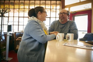 A couple looking into each other's eyes while sitting at a counter with coffee cups