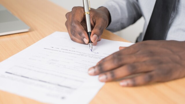 Man's hands signing a paper on a desk